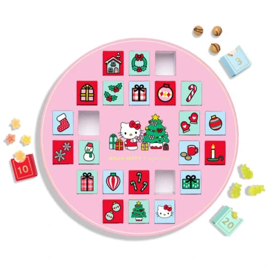 A circular Hello Kitty advent calendar with a pink background. It features a grid of colorful doors, some open to reveal candies, decorated with festive icons like gifts, a Christmas tree, candy canes, and stockings. Small candies are scattered around the calendar.