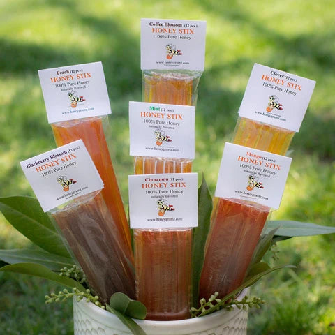 Honey sticks in a decorative pot with visible labels against a blurred green background