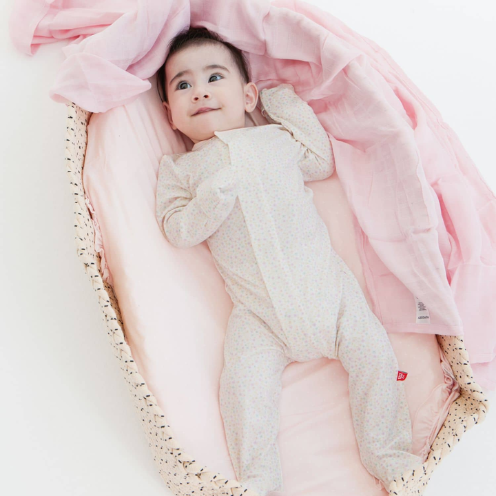 Baby in a white onesie lying on pink fabric