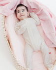 Baby in a white onesie lying on pink fabric