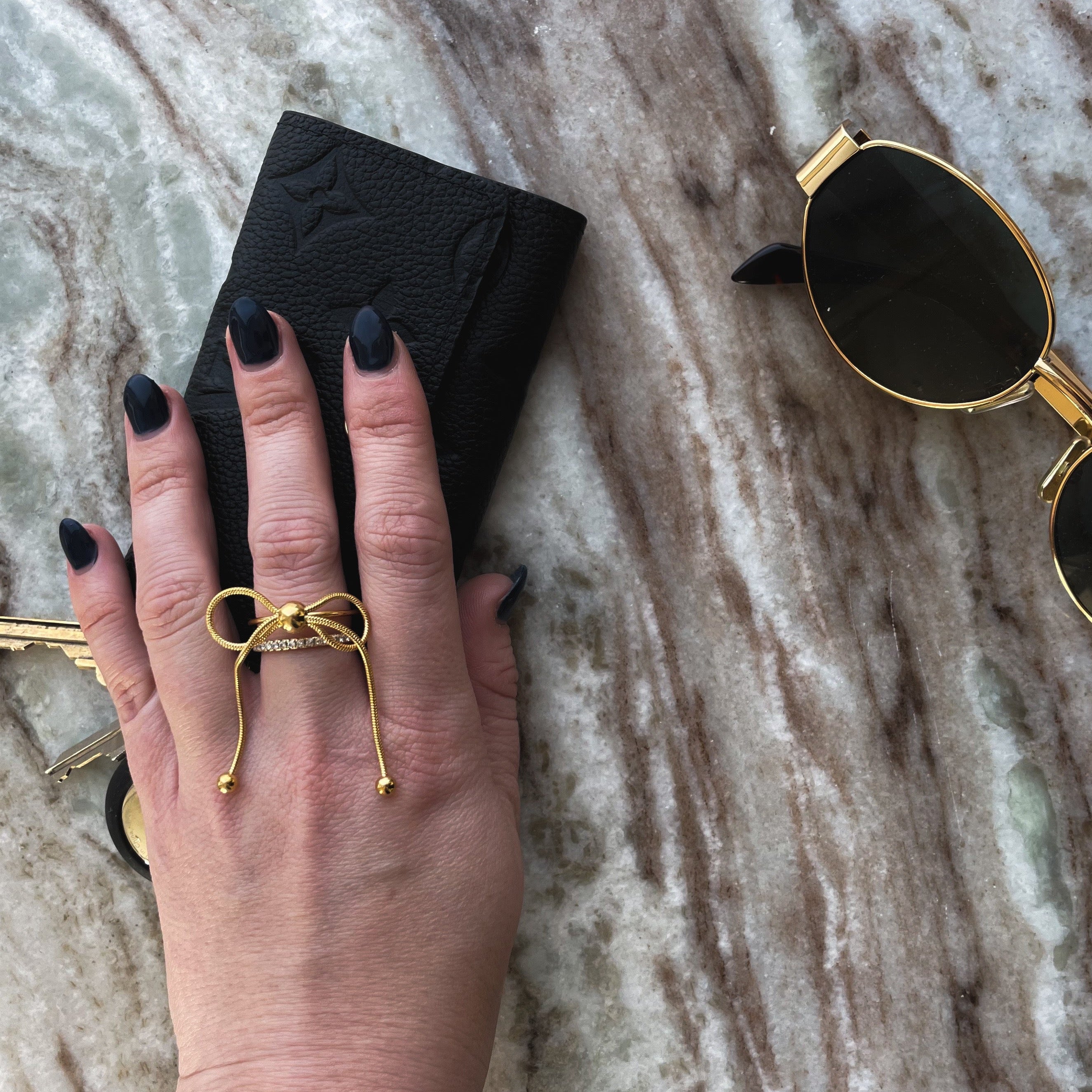 Gold bow ring on hand grabbing wallet and sunglasses