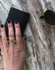 Gold bow ring on hand grabbing wallet and sunglasses