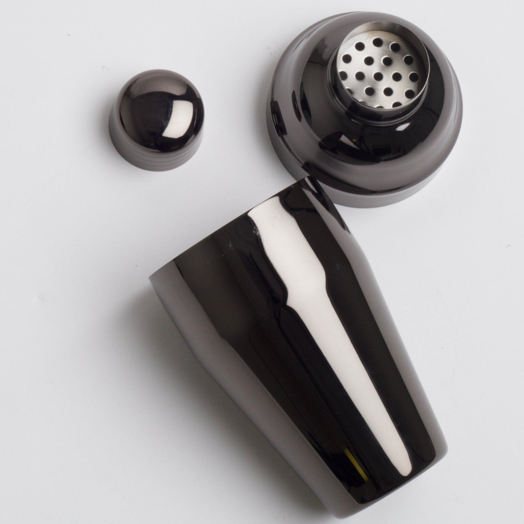 gunmetal cocktail shaker, now disassembled into three parts: the base, the built-in strainer, and the cap, revealing the inner components.