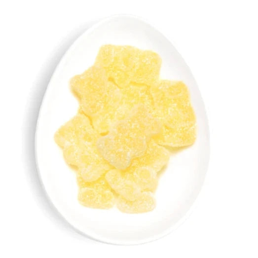 A white, oval-shaped dish containing a pile of yellow, bear-shaped gummy candies. The candies are lightly dusted with sugar, giving them a sparkly appearance.