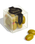 A clear, cube-shaped box containing candy-coated almonds designed to look like green olives with a red center. The black and gold label reads "Chopin Martini Olive Almonds - Sugarfina." Two "olive" candies are placed outside the box.