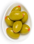 A small, white, oval-shaped dish holding several candy-coated almonds styled as green olives with red detailing to mimic pimentos.