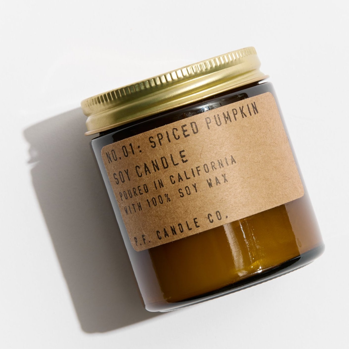 An orange candle with a gold lid with the description of, &quot; NO. 01: SPICED PUMPKIN SOY CANDLE,&quot; poured in California with Soy Wax, on a white background