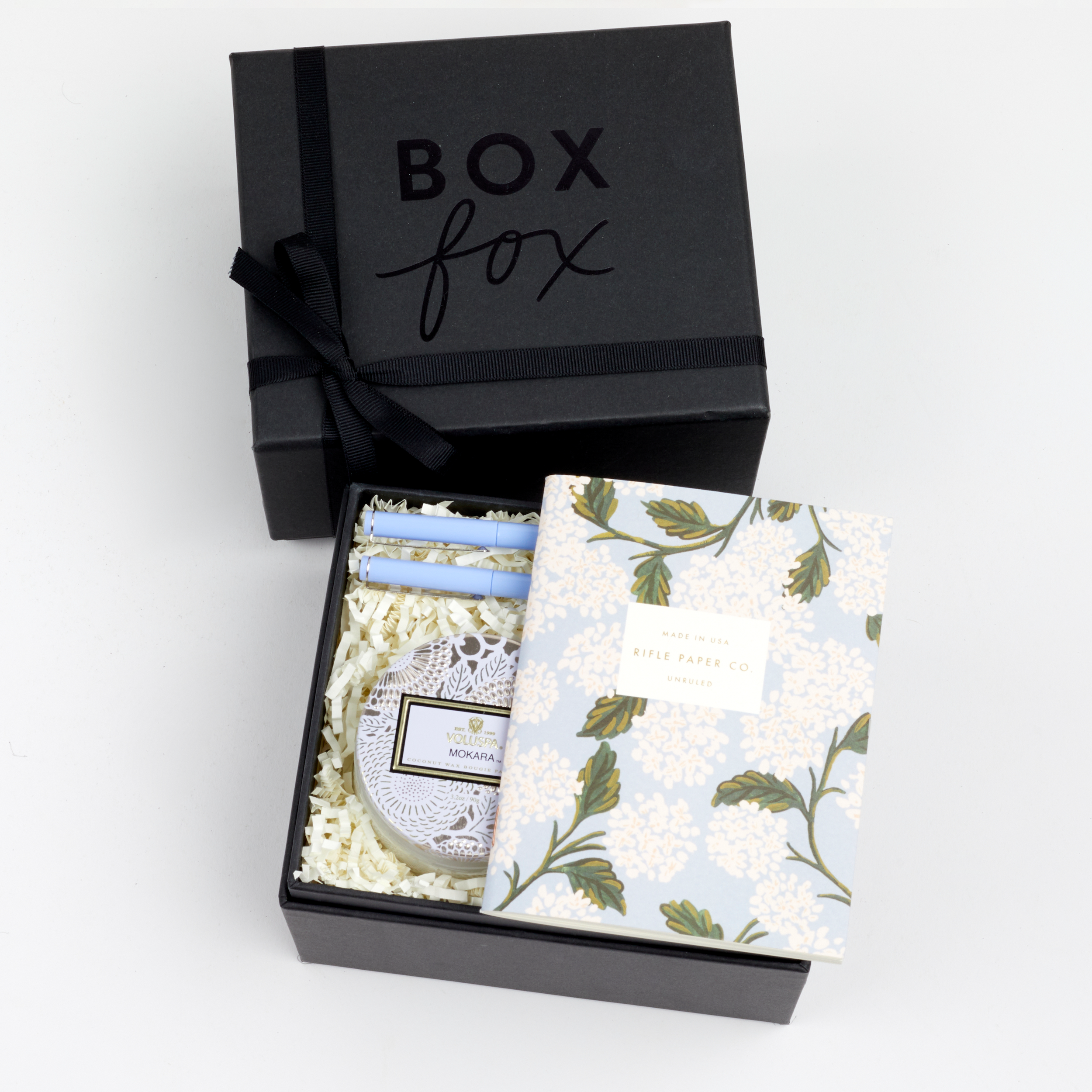 BOXFOX black Gift Box containing Rifle Paper Hydrangea Pocket Notebooks, 2 Periwinkle Le Pens, and Voluspa Mokara Petite Glass Jar Candle.