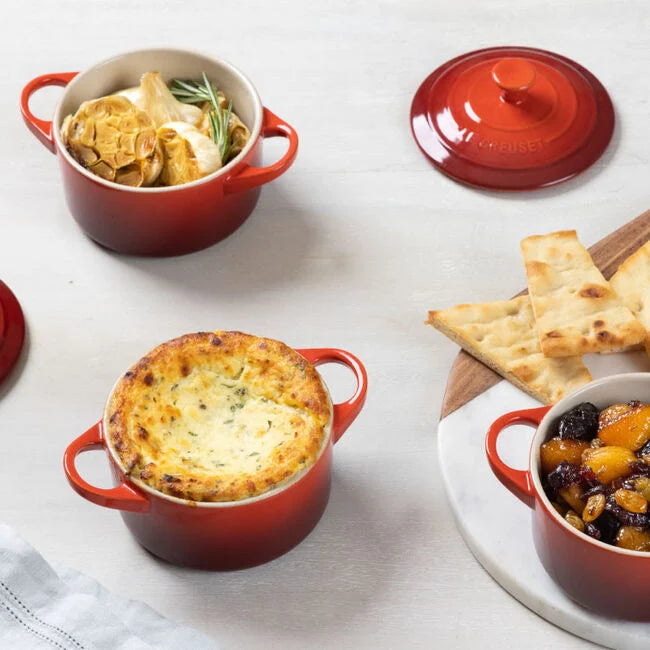 Red ceramic cookware with various dishes on a light surface