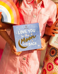 Children holding a 'Love You to the Moon and Back' book with colorful backgrounds