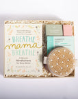 A curated gift box set for busy moms, featuring a book titled 'Breathe Mama Breathe' by Shonda Mensha, a peppermint eucalyptus diffuser, a pink bath bomb, and a natural cell resurfacer eye mask, all arranged in a kraft paper box with shredded paper filler on a white background.