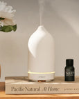 White Stone Essential Oil Diffuser sits on top of book next to Sleep oil and vase of flowers