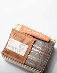 A curated gift box set on a clean white background, featuring a tea packet labeled 'TEA WITH ME', a peach-colored lip balm tube from 'ear beauty', and a plaid book or booklet titled 'PUMPKIN WHISPER'.