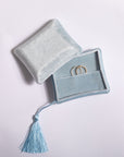 A light blue velvet ring pouch with a matching tassel, shown partially open with two gold rings inside on a plain light background.