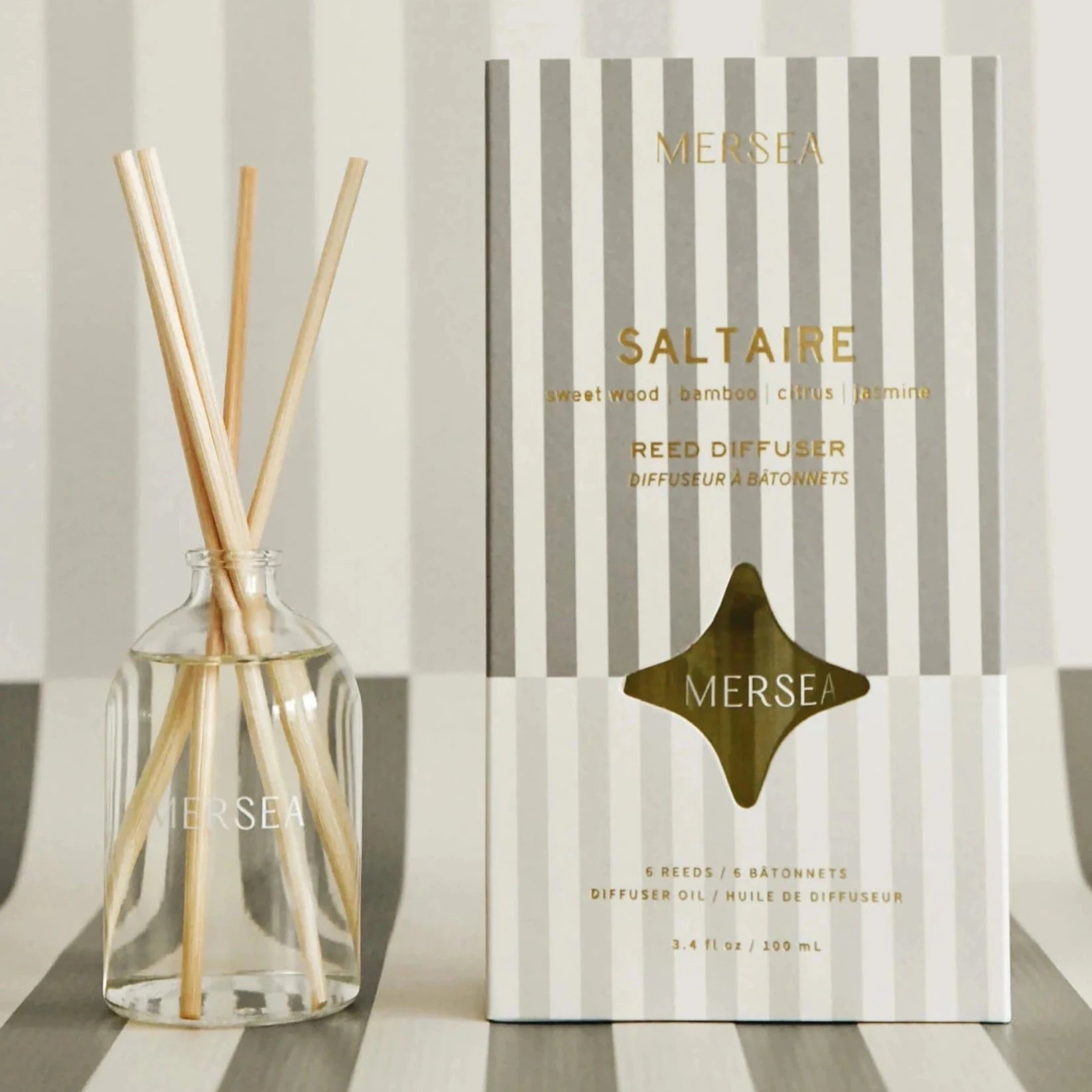 gray vertically striped box with gold text. next to it is reed diffuser