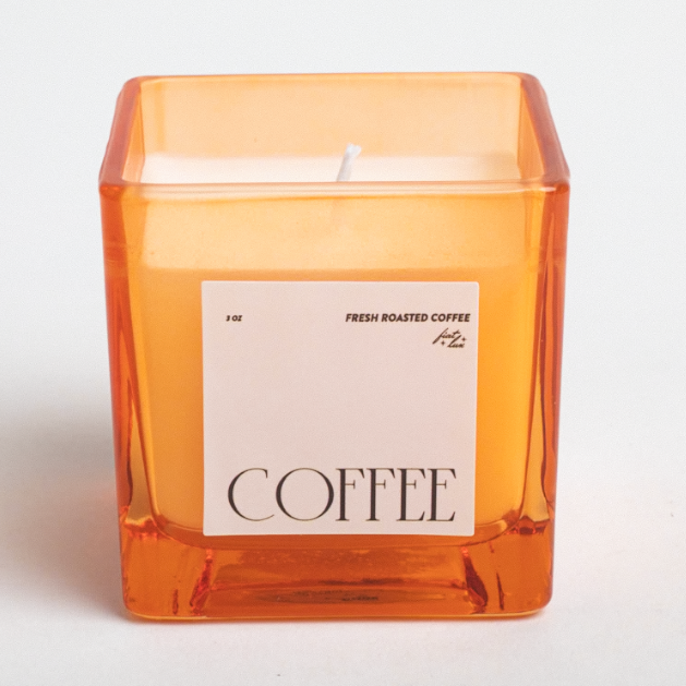 Candle in an orange glass container with a 'Coffee' label on a white background