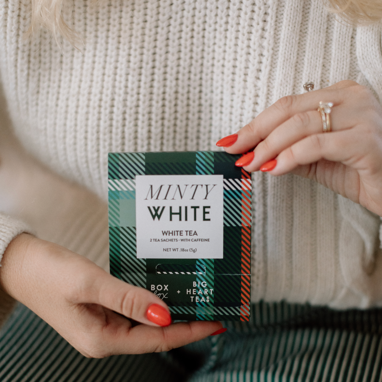 Person holding a box of 'Minty White' white tea with a plaid pattern.