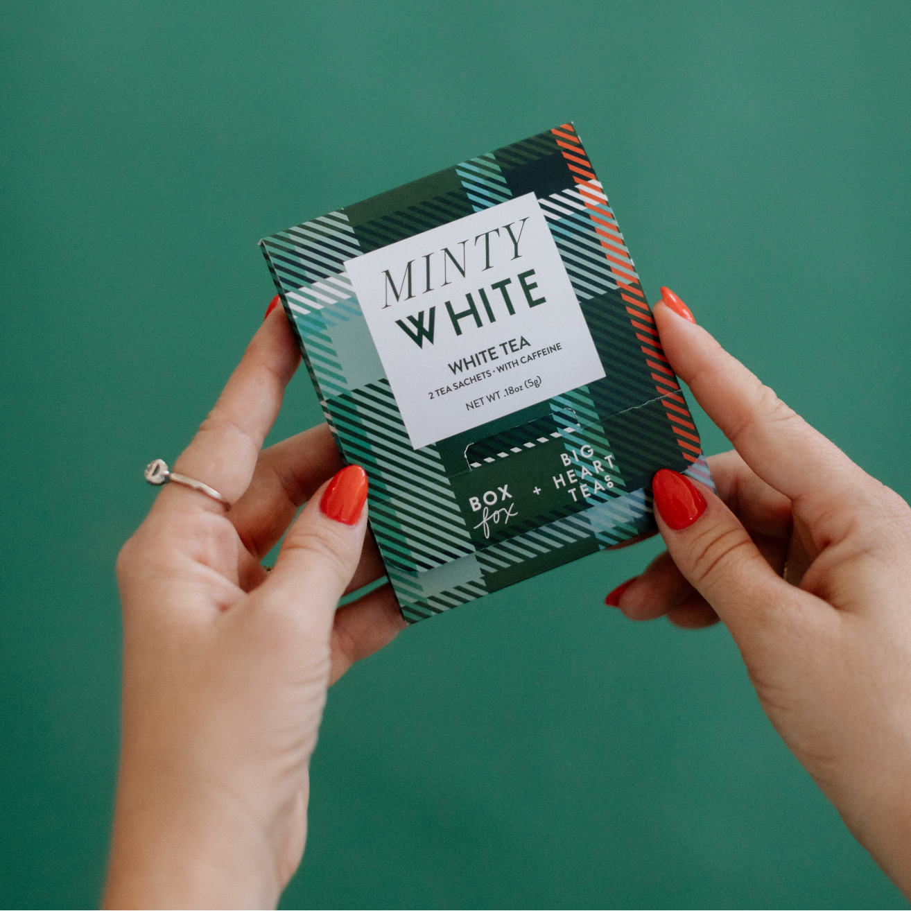 Person holding a box of 'Minty White' white tea against a green background