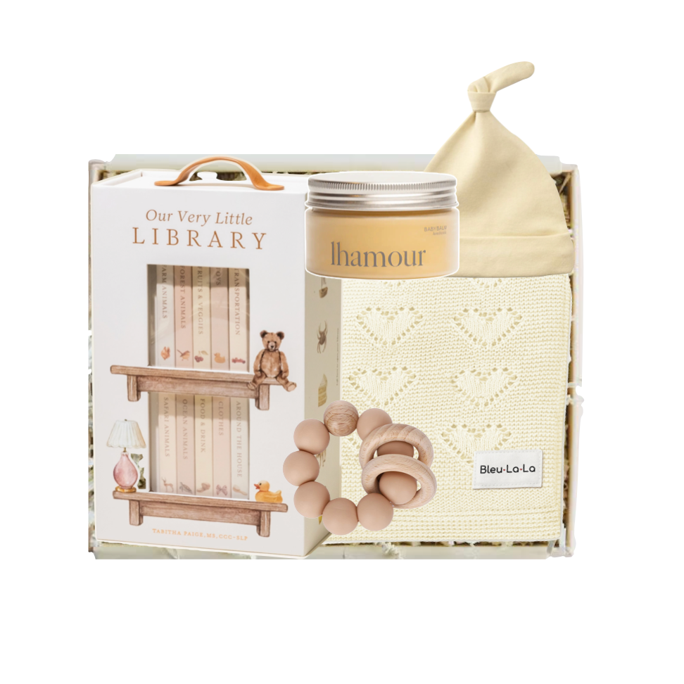 Baby product set with 'Our Very Little Library' packaging, including a bottle, bib, and rattle.