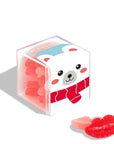 A small transparent cube-shaped box filled with red and pink sugar coated candies shaped like lips. The box is decorated with a cute polar bear wearing a red scarf. Two candies are placed outside the box for display.