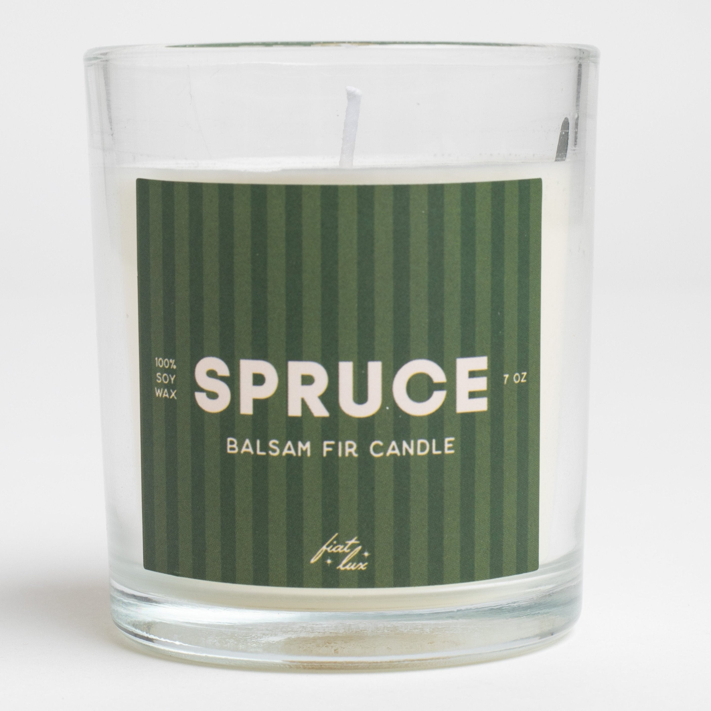 A candle labeled "SPRUCE" with "Balsam Fir Candle" and "100% Soy Wax" noted on the label. The candle appears to have a forest green, striped label. 