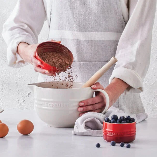 Person adding ingredients to a mixing bowl with a white background