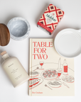 Table for Two ready to ship products including "Table for Two" cookbook, Le Creuset spoon rest, Branche olive oil, Maldon Chili Salt, and marble salt cellar