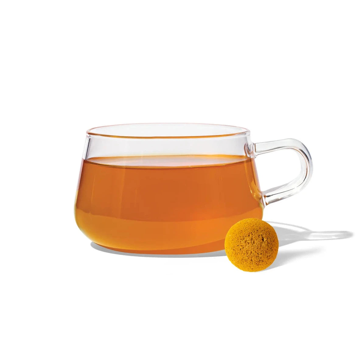 clear glass mug with golden tea. yellow round tea drop is in front of it 