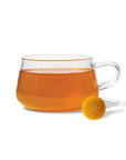 clear glass mug with golden tea. yellow round tea drop is in front of it 