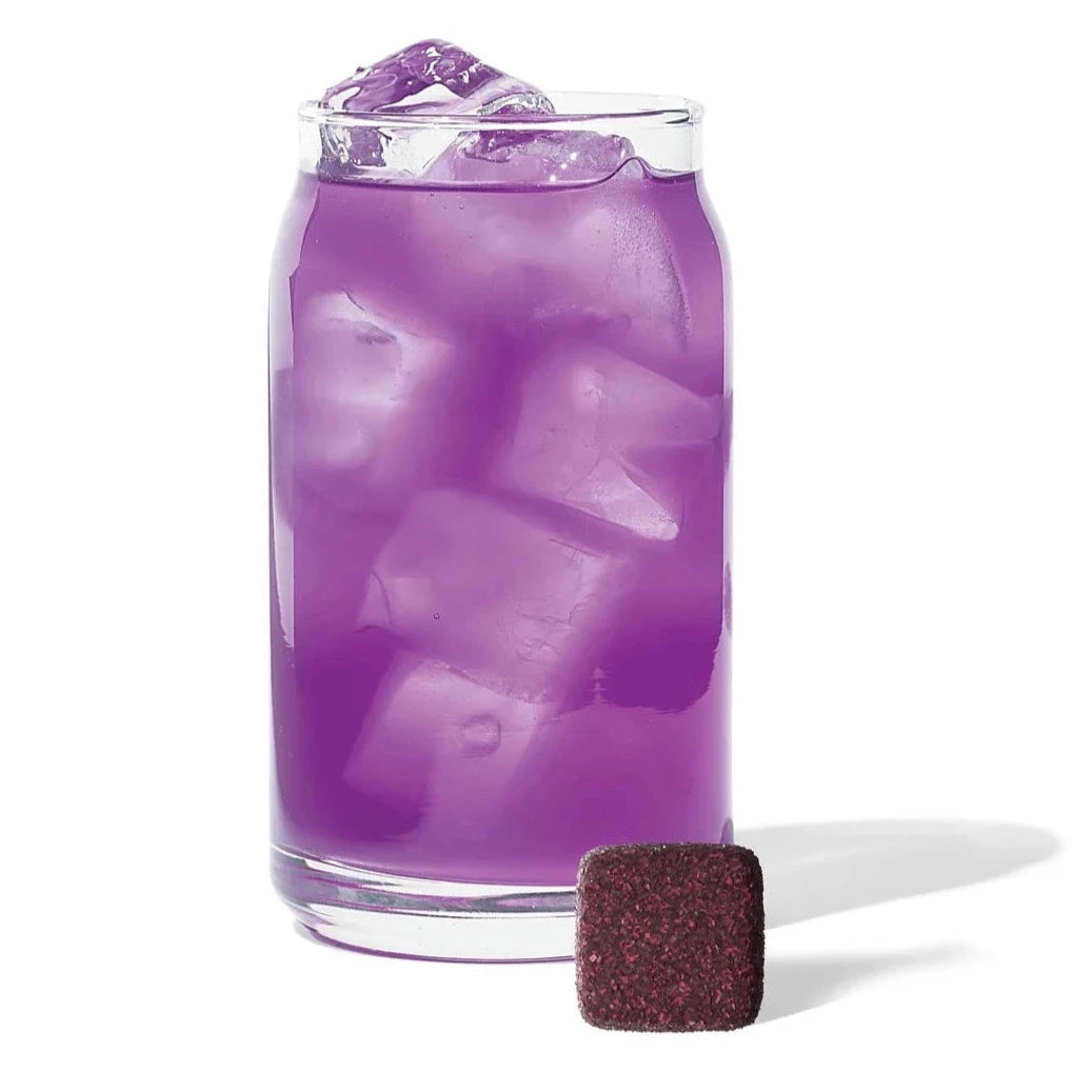 clear glass cup with purple tea inside. in front of it is a purple compressed tea cube