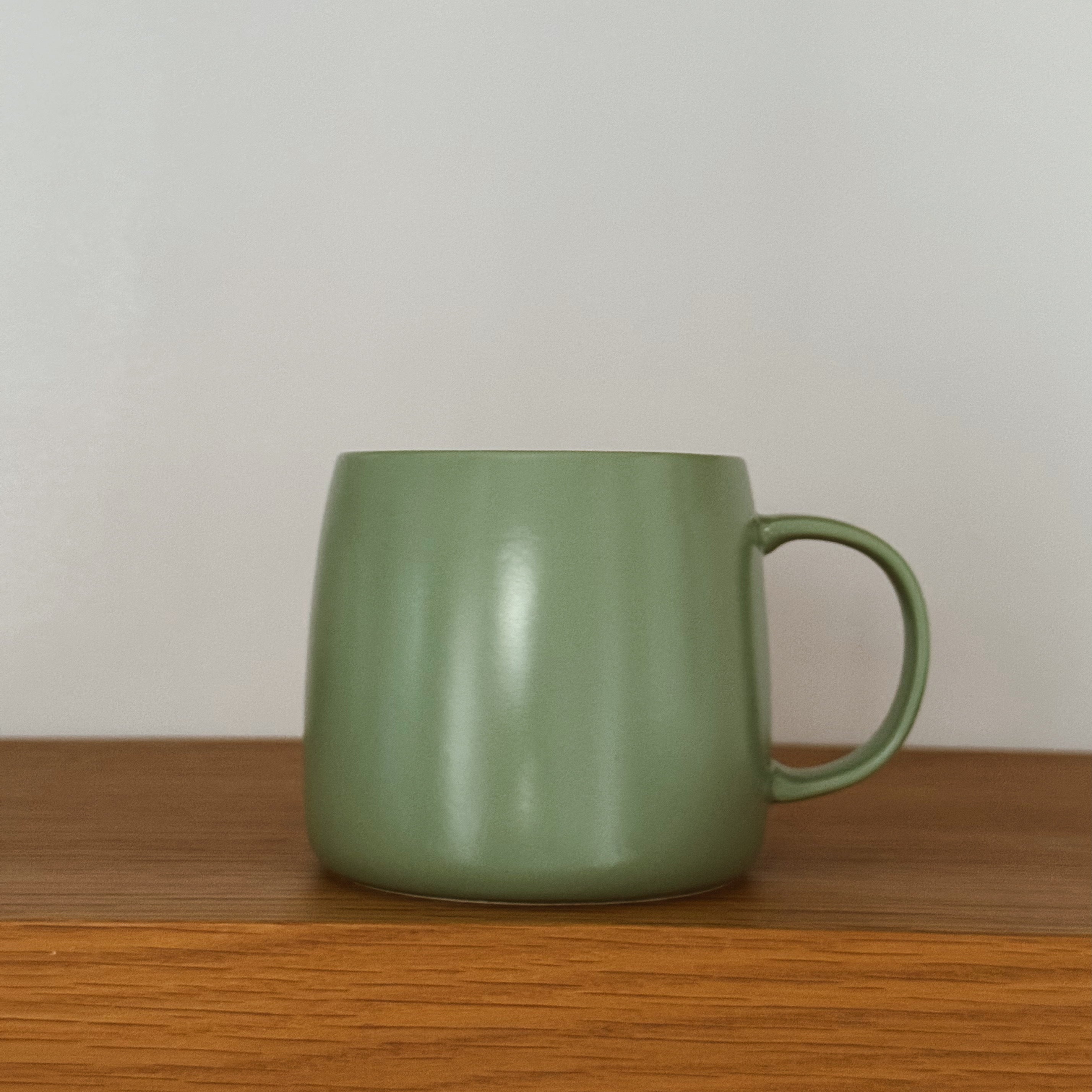 Green mug on a wooden surface with a plain background