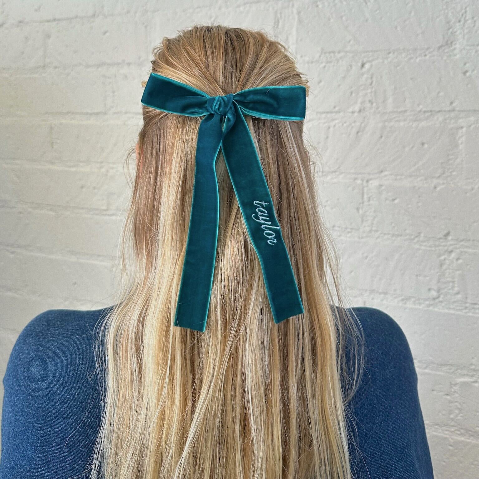 Person with teal ribbon in hair against a white brick wall