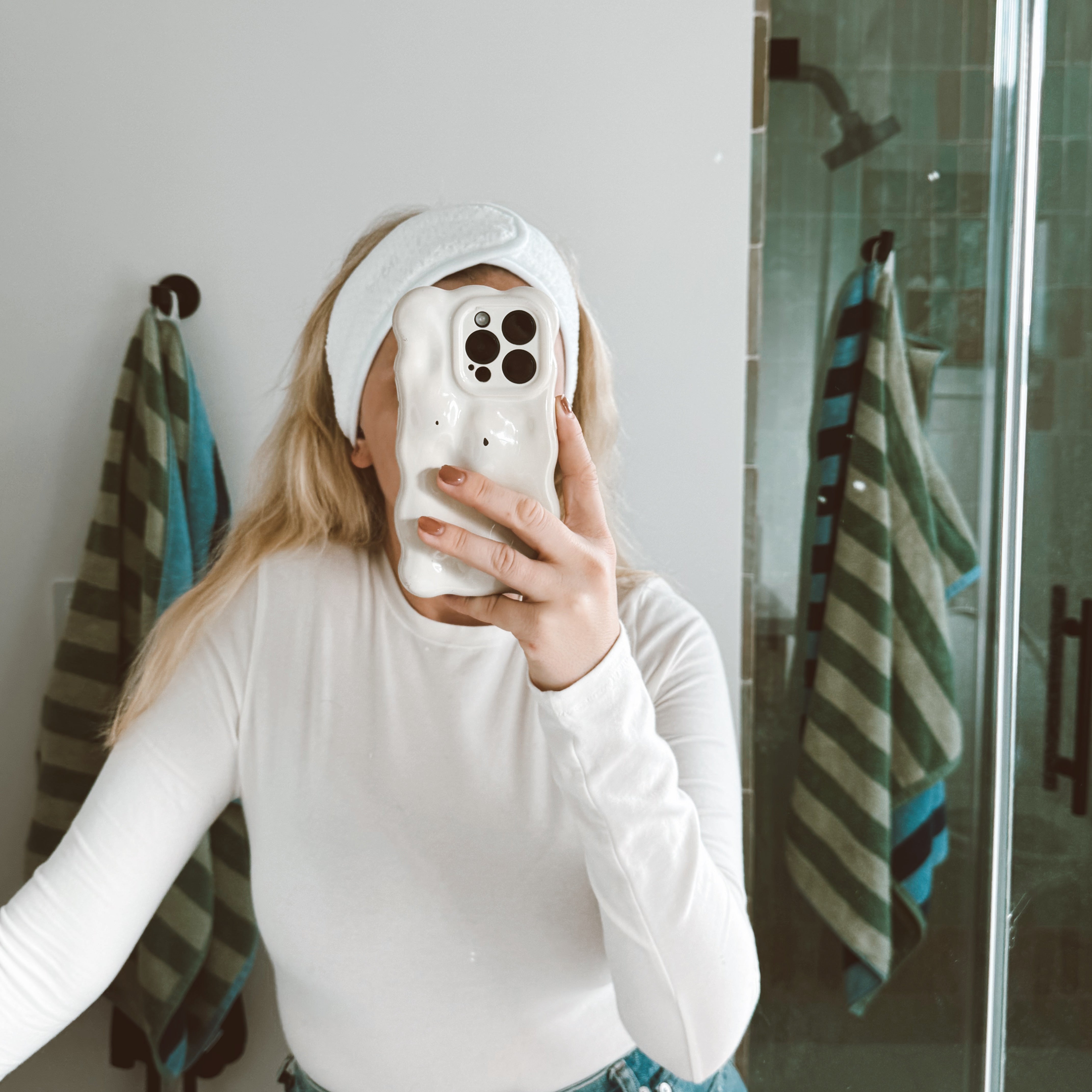 girl wearing white spa headband and taking a selfie in the bathroom mirror with her phone