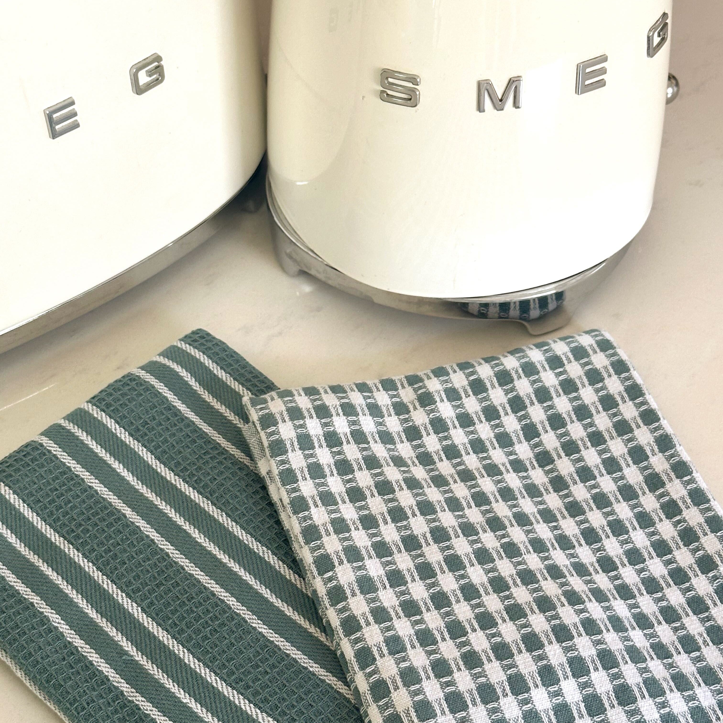 Two green kitchen towels on a countertop with a Smeg appliance in the background.