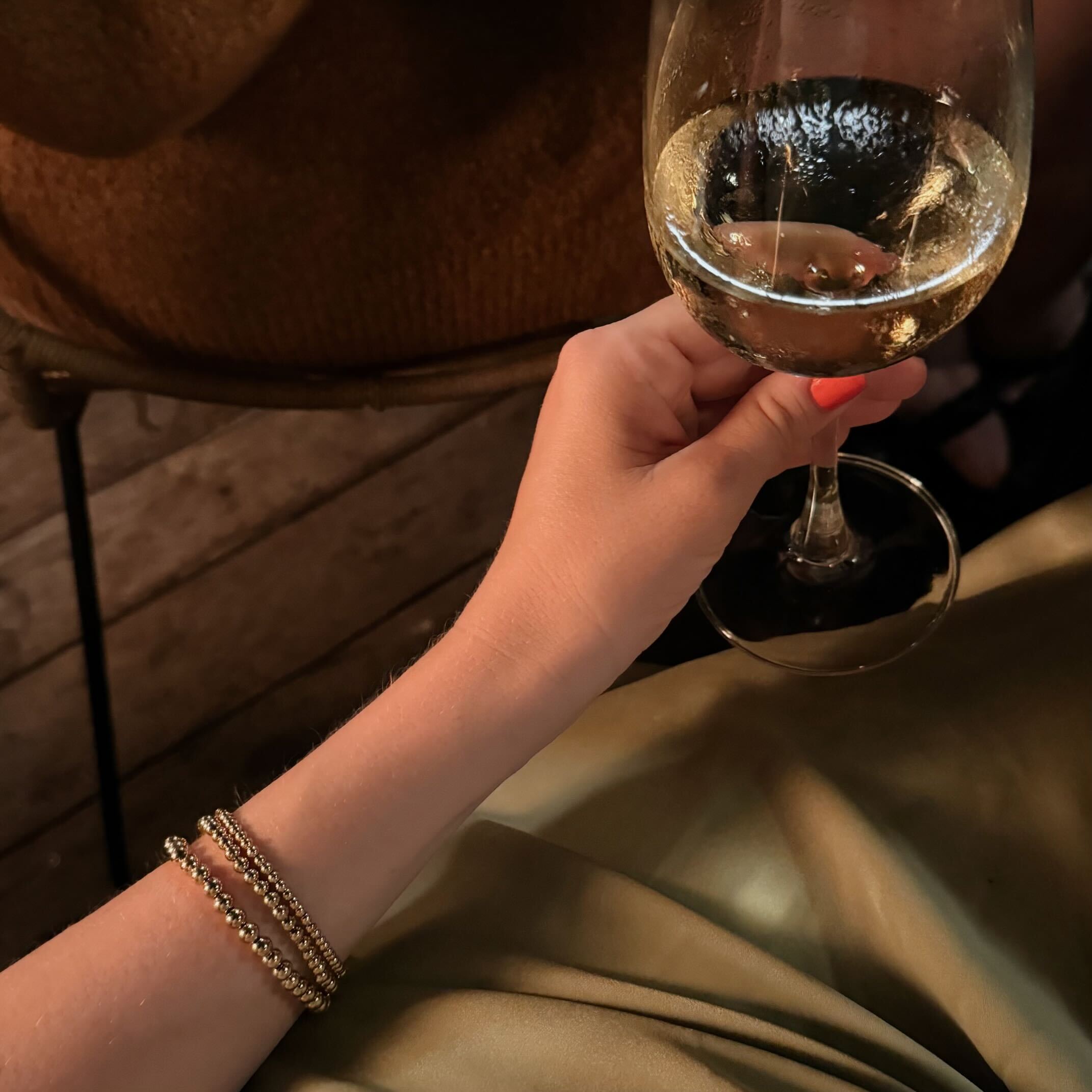 gold beaded bracelet set on wrist holding a glass of wine