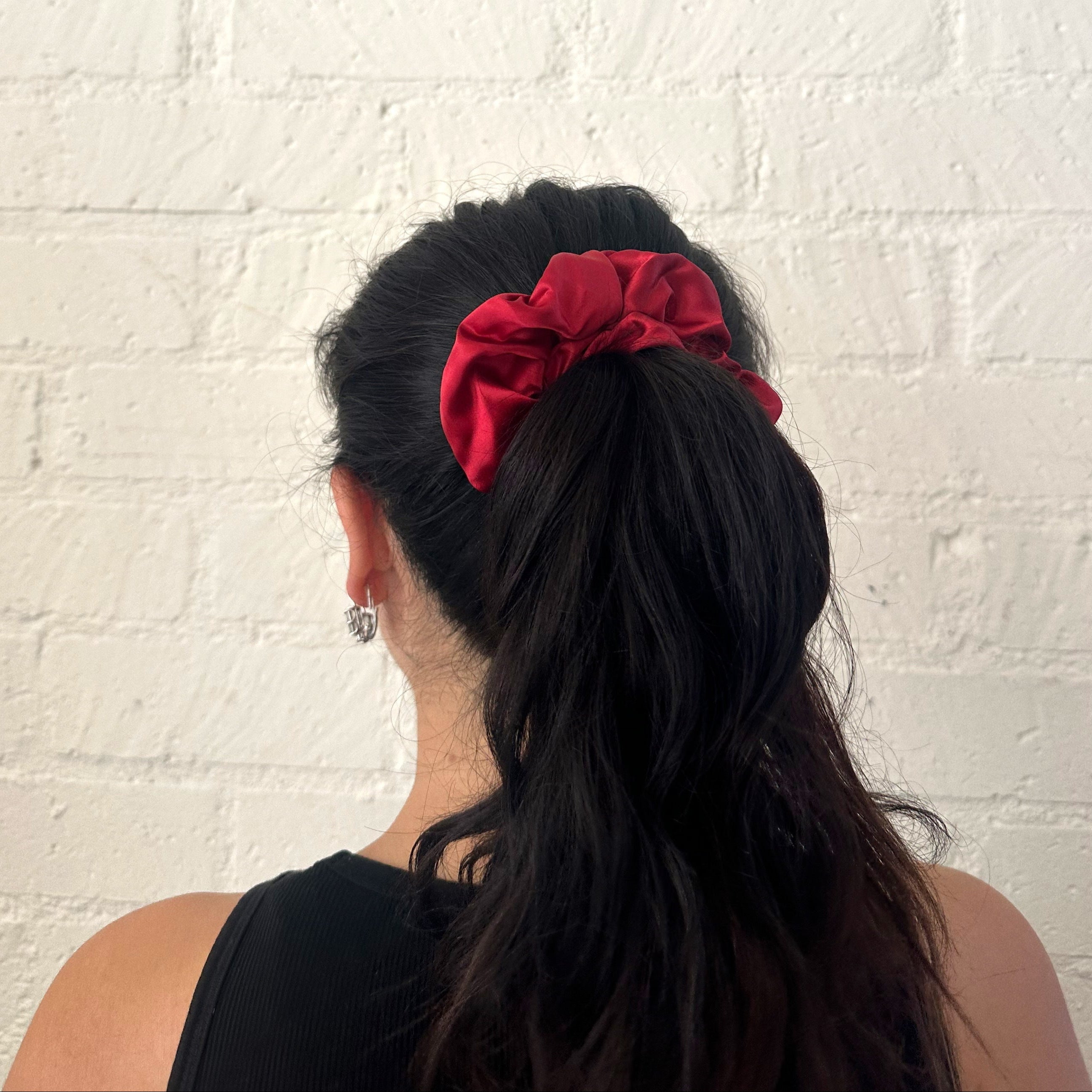 Person with a high ponytail wearing a red scrunchie against a white brick wall.