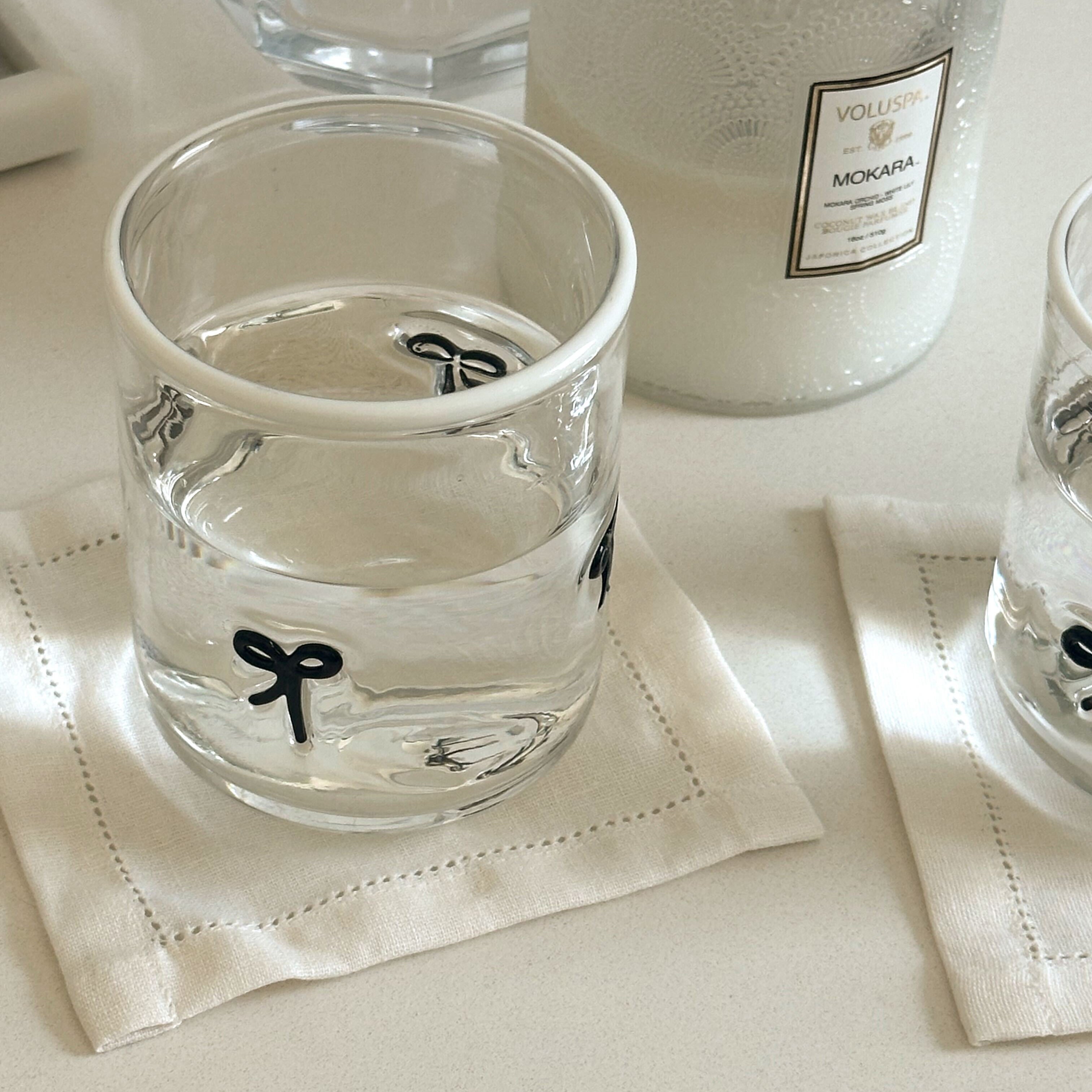 Clear glass with black bow design on a white napkin, next to a bottle of Veuve Clicquot champagne.
