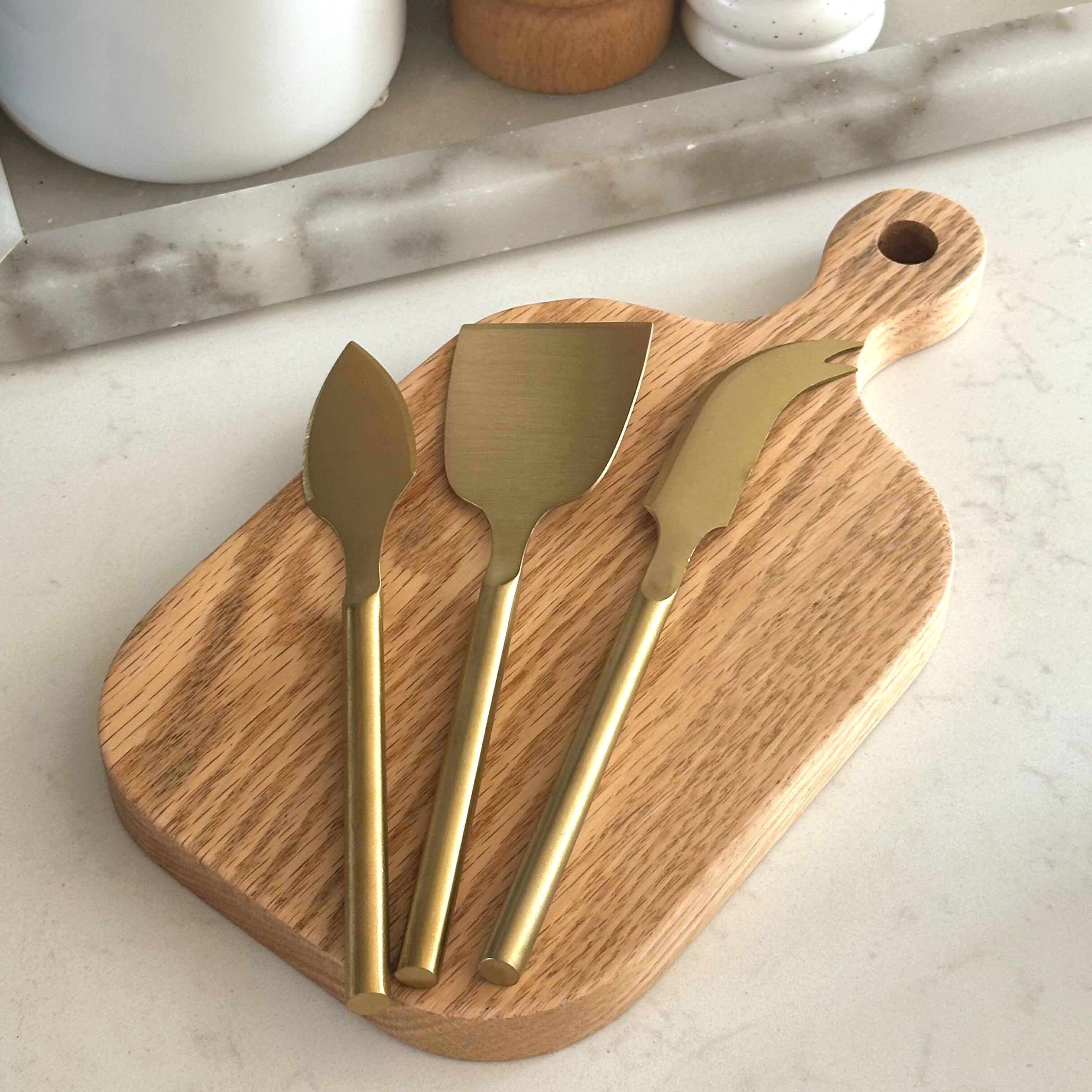 Wooden cutting board with gold cheese knives on a marble surface