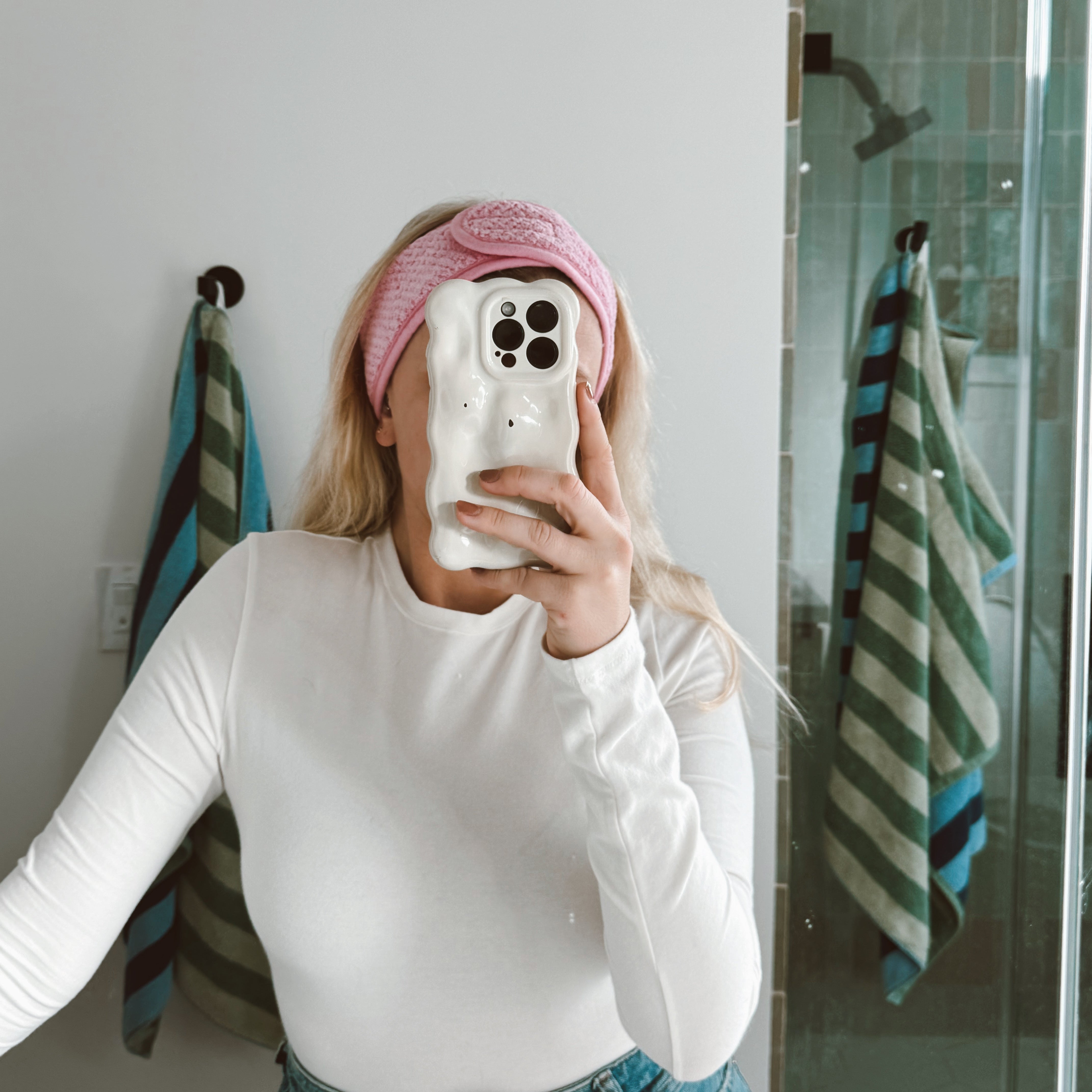 girl wearing pink spa headband and taking a selfie in the bathroom mirror with her phone