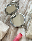 Compact mirror, pink lip balm, and Gucci wallet on a marble surface