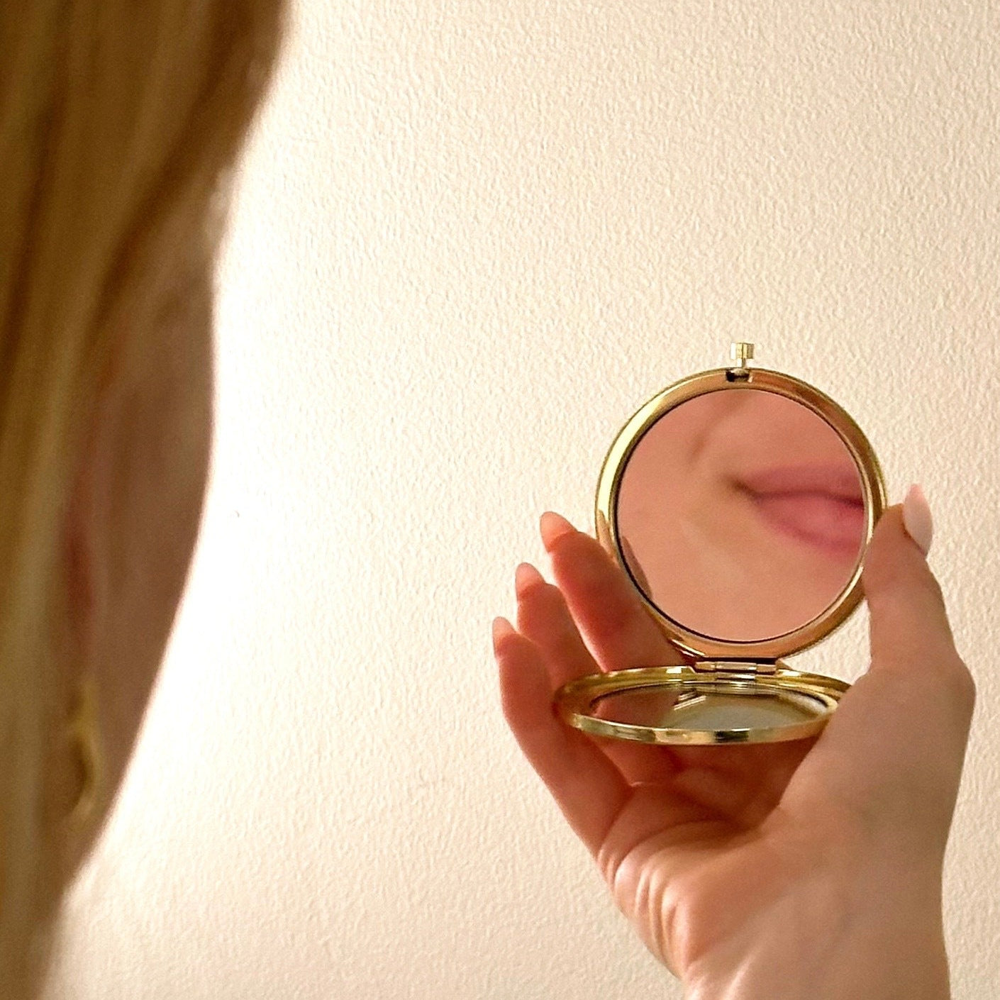 Hand holding a gold compact mirror against a plain background