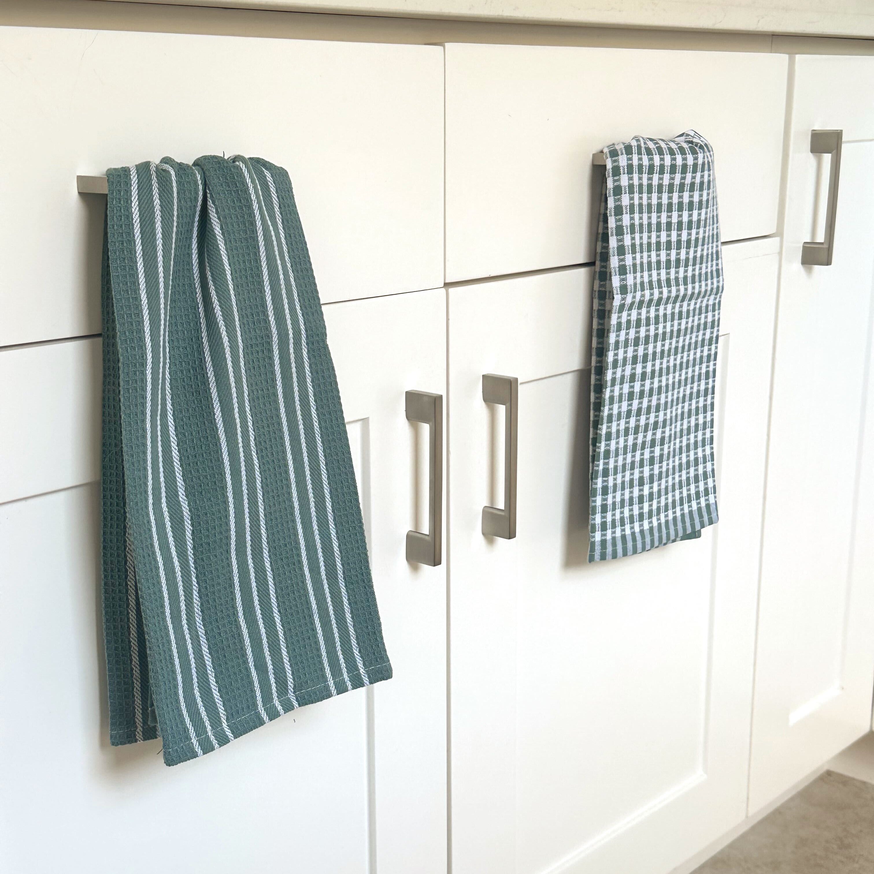 Green and white checkered towels hanging on a kitchen cabinet.