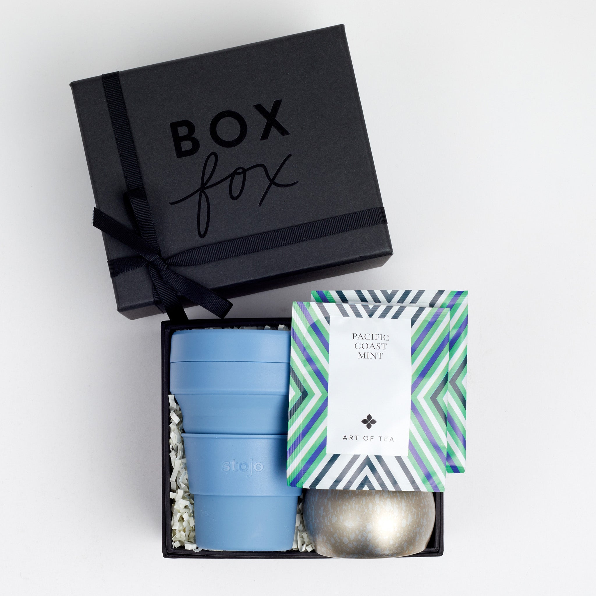Black BOXFOX gift box next to open box including collapsible cup, tin candle and two art of tea sachets