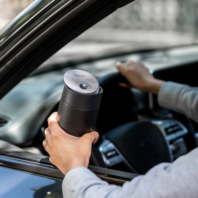 Person holding a black thermos while sitting in a car