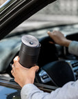 Person holding a black thermos while sitting in a car