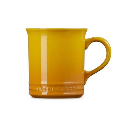 A yellow Le Creuset ceramic mug with a handle, shown on a plain white background.