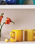 Two yellow mugs on a shelf with a vase of flowers and a lemon.