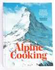 A hardcover book with photo of snow covered mountain peak on cover with red text that reads, "Alpine Cooking" photographed on white background.