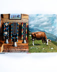 Alpine Cooking opened to left page showing three silver hanging bells with embroidered straps in a ranch, and the right showing a cow grazing in a field with text over the image describing the cattle procession. 