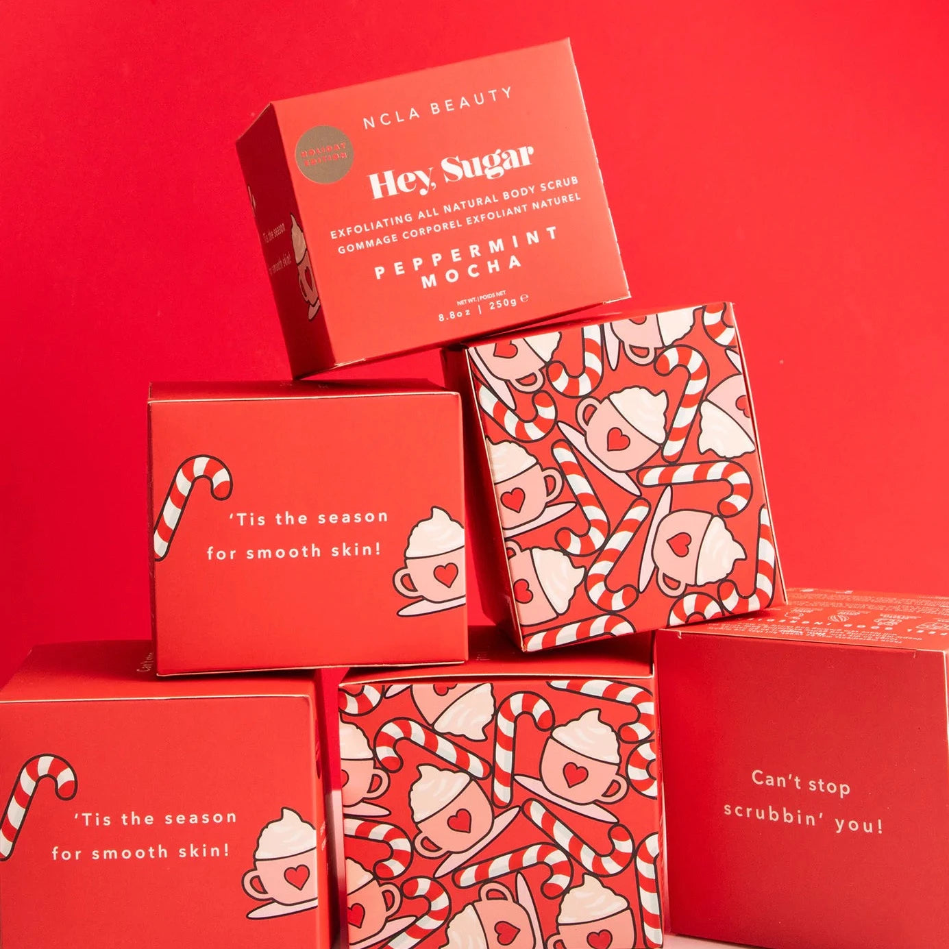 red box packaging for the Hey Sugar Peppermint Mocha Body Scrub. Box is red in the from with white text. Sides of boxes have cups of peppermint mocha printed on them along with candy canes